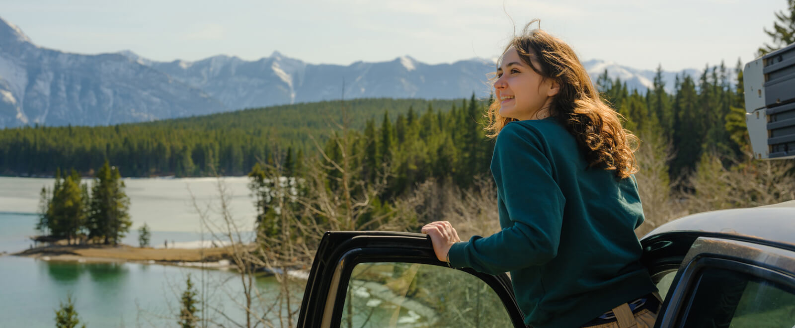 A young woman stading up from her car and looking out toward mountains