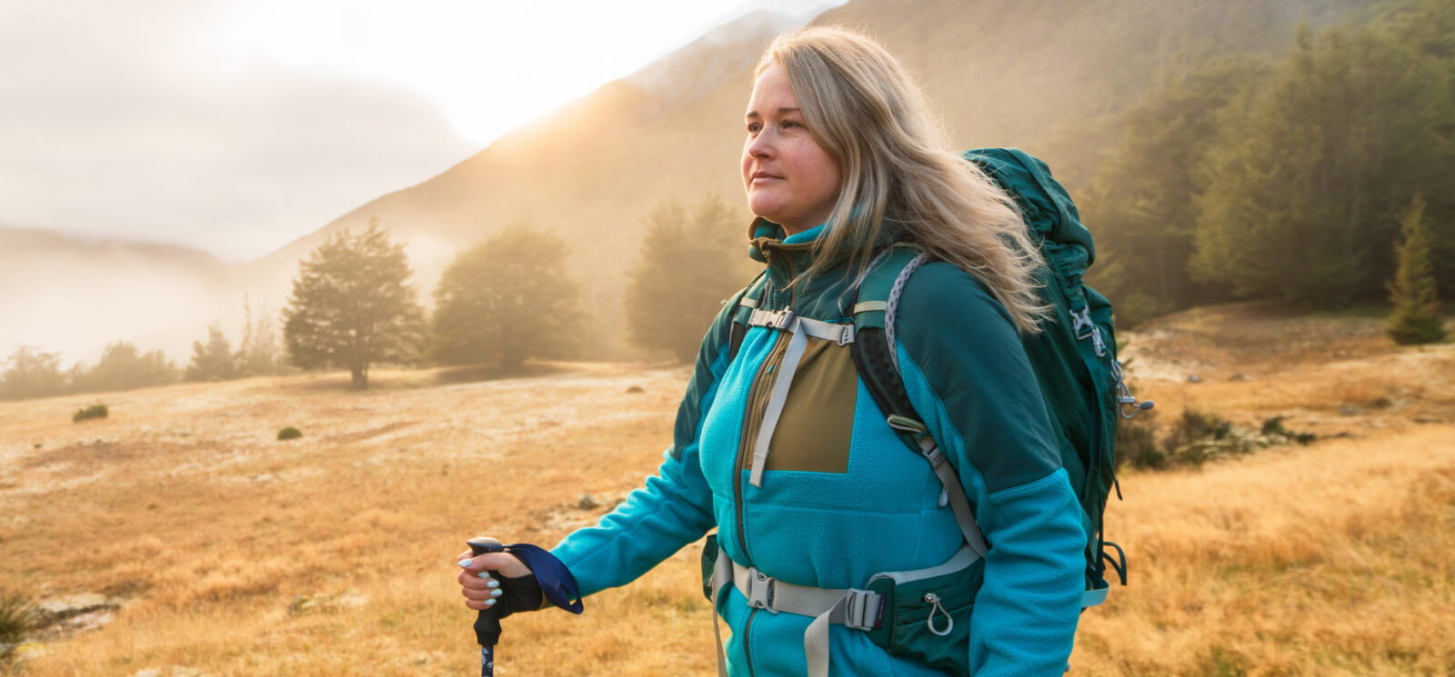 A woman hiking with the sun setting behind a mountain