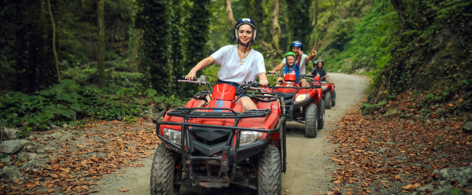 A family riding several ATVs on a wooded path