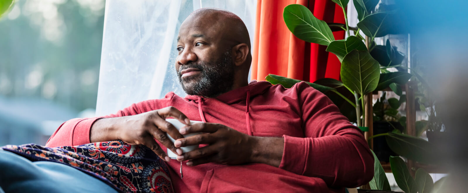 A man holding a coffee cup and looking out a window 